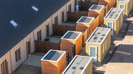 Rij nieuwbouwwoningen met donkere zadeldaken en meerdere houten bergingen in de achtertuinen, gezien vanuit een verhoogd perspectief.